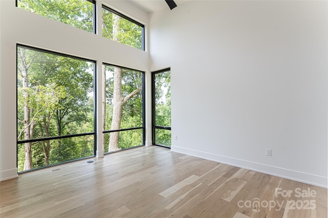 empty room featuring light wood-type flooring, a high ceiling, and baseboards