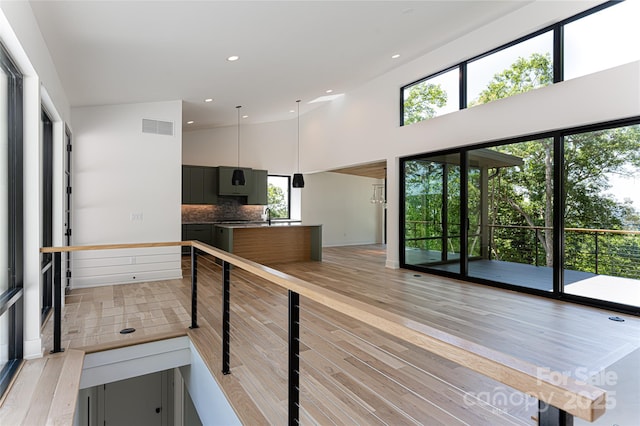 kitchen with a towering ceiling, light wood finished floors, tasteful backsplash, and visible vents