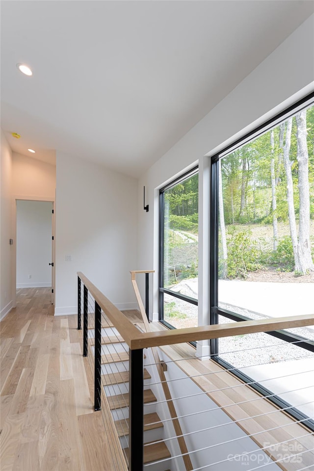 corridor with light wood-type flooring, recessed lighting, lofted ceiling, and an upstairs landing