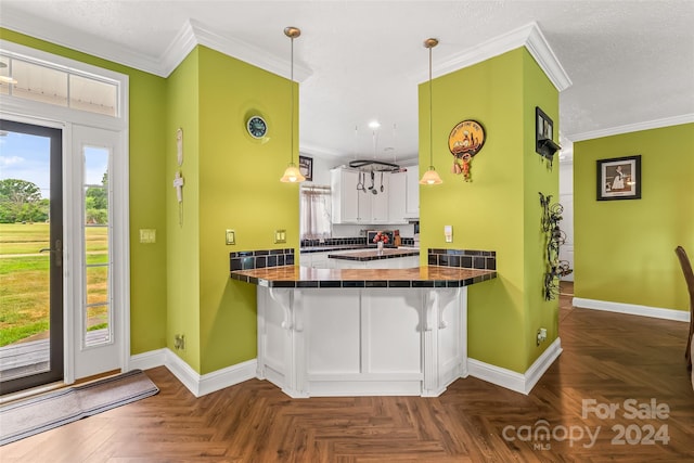 kitchen with kitchen peninsula, a kitchen breakfast bar, ornamental molding, dark parquet floors, and white cabinets