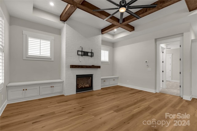 unfurnished living room with beam ceiling, ceiling fan, a fireplace, light hardwood / wood-style floors, and coffered ceiling