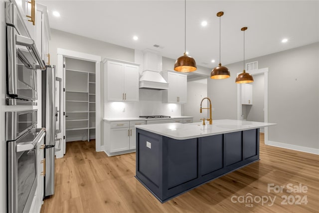 kitchen featuring custom exhaust hood, appliances with stainless steel finishes, white cabinetry, light hardwood / wood-style flooring, and decorative light fixtures