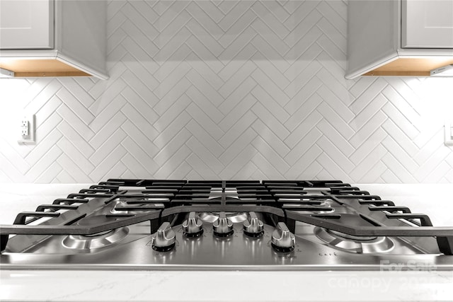 details featuring white cabinetry, stainless steel gas cooktop, and backsplash