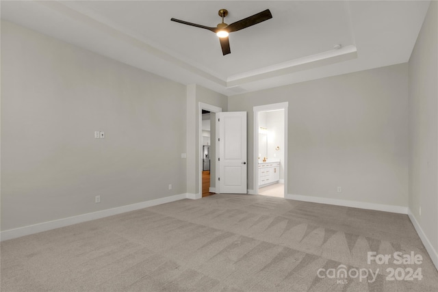 unfurnished bedroom featuring connected bathroom, ceiling fan, a raised ceiling, and light carpet