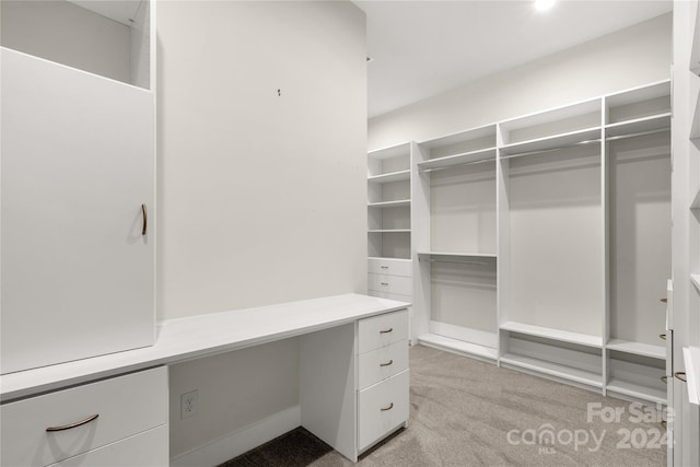 spacious closet featuring built in desk and light carpet