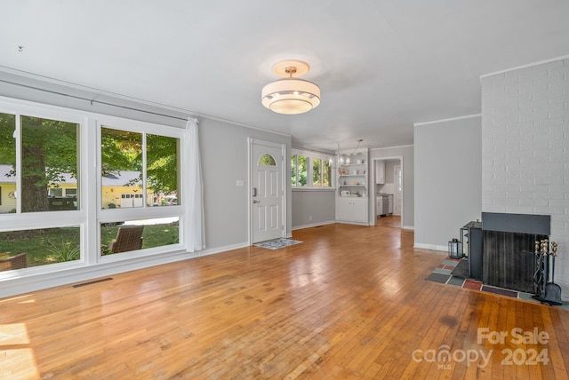 unfurnished living room featuring hardwood / wood-style floors, a brick fireplace, and crown molding