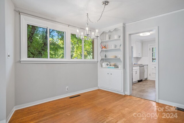 unfurnished dining area with crown molding, a chandelier, and light wood-type flooring