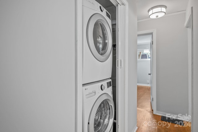 laundry room with crown molding, stacked washer / drying machine, and wood-type flooring