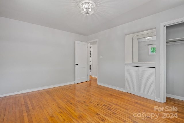 unfurnished bedroom with a notable chandelier, a closet, stacked washer and clothes dryer, and light hardwood / wood-style floors