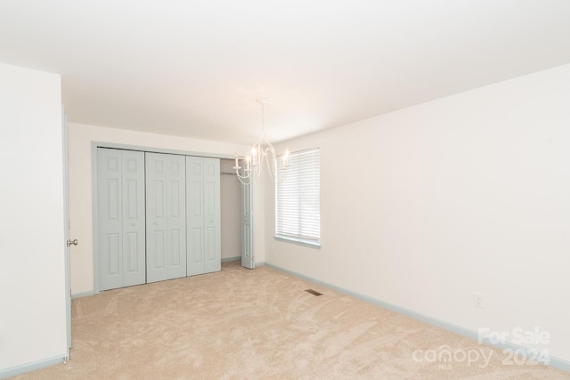 unfurnished bedroom featuring a closet, light colored carpet, and a chandelier