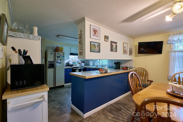 kitchen with white refrigerator with ice dispenser, backsplash, stainless steel range with electric cooktop, blue cabinets, and a textured ceiling