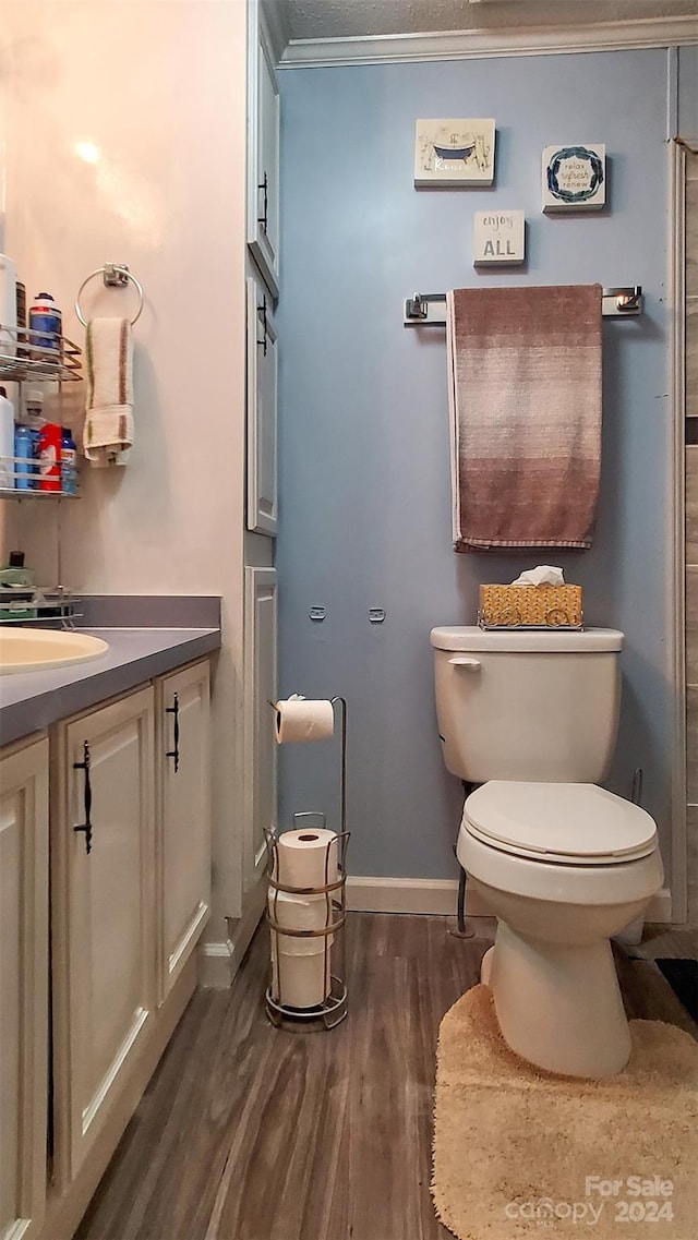 bathroom with toilet, hardwood / wood-style floors, vanity, and ornamental molding