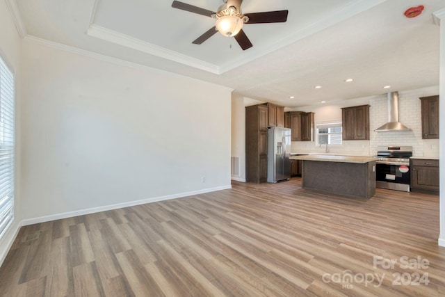 kitchen featuring appliances with stainless steel finishes, light wood-type flooring, wall chimney range hood, a kitchen island, and crown molding