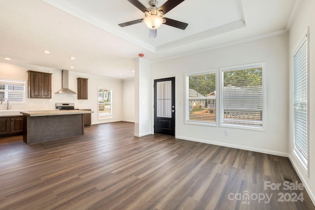 unfurnished living room featuring dark hardwood / wood-style flooring, sink, ceiling fan, a tray ceiling, and crown molding