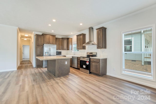 kitchen with wall chimney exhaust hood, a kitchen island, stainless steel appliances, tasteful backsplash, and light wood-type flooring