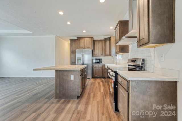 kitchen with hardwood / wood-style floors, stainless steel appliances, backsplash, wall chimney range hood, and a center island