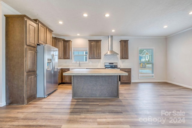 kitchen featuring stainless steel appliances, crown molding, a center island, and wall chimney range hood