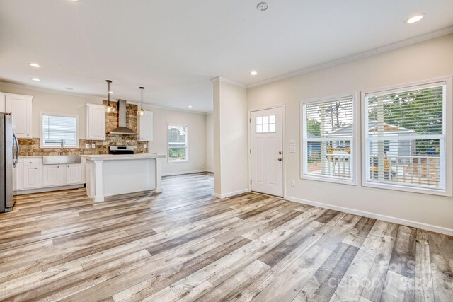 kitchen featuring a center island, hanging light fixtures, wall chimney range hood, and plenty of natural light