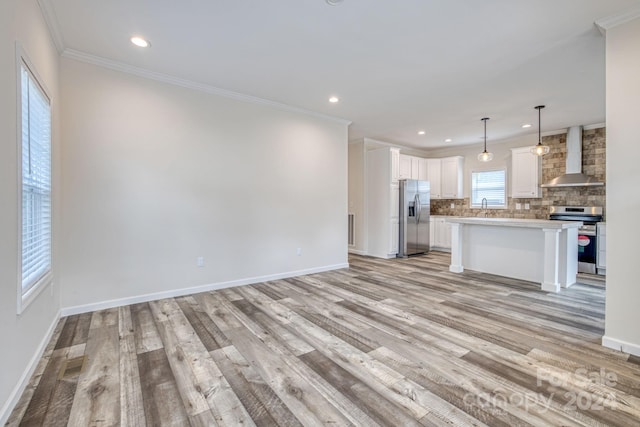 kitchen featuring appliances with stainless steel finishes, white cabinets, pendant lighting, a center island, and wall chimney range hood