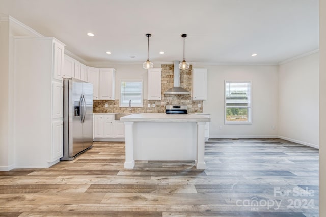 kitchen with wall chimney exhaust hood, white cabinets, appliances with stainless steel finishes, and light wood-type flooring