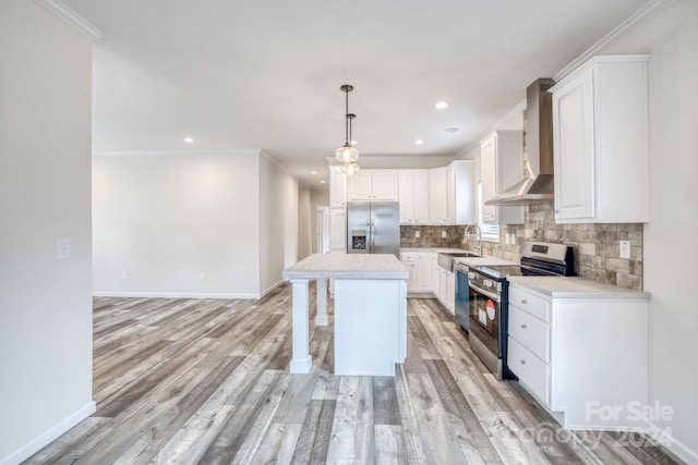 kitchen featuring hanging light fixtures, a kitchen island, wall chimney exhaust hood, white cabinetry, and appliances with stainless steel finishes