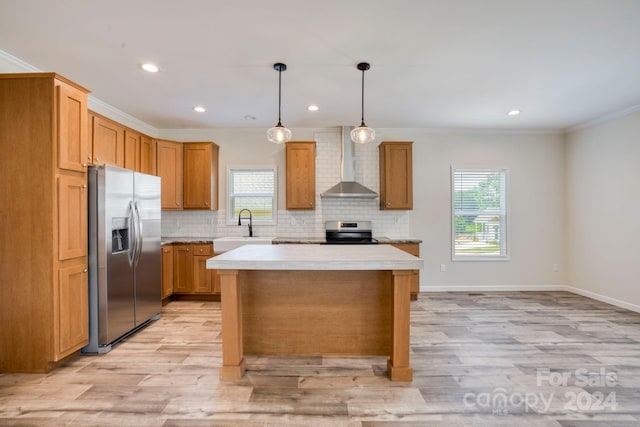 kitchen featuring light hardwood / wood-style floors, a kitchen island, wall chimney range hood, appliances with stainless steel finishes, and decorative light fixtures