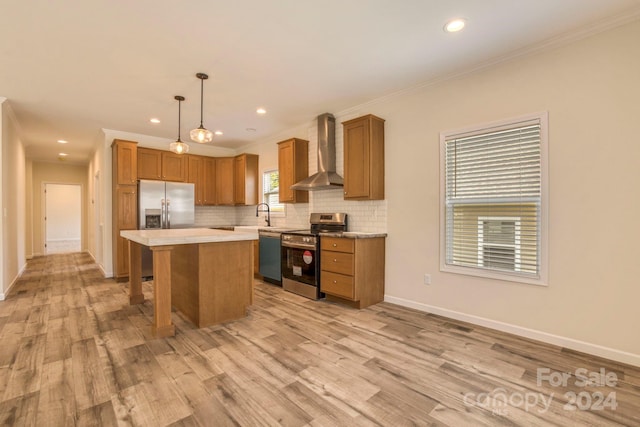 kitchen featuring hanging light fixtures, light hardwood / wood-style flooring, wall chimney range hood, appliances with stainless steel finishes, and a center island