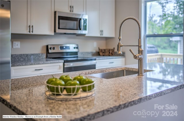 kitchen with white cabinets, stainless steel appliances, sink, and light stone counters