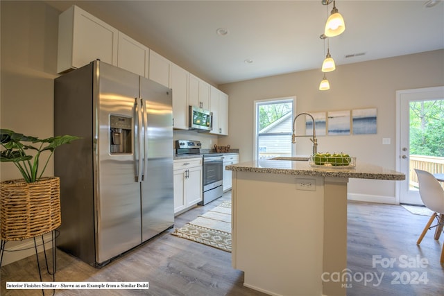 kitchen featuring stainless steel appliances, an island with sink, light hardwood / wood-style flooring, white cabinets, and pendant lighting