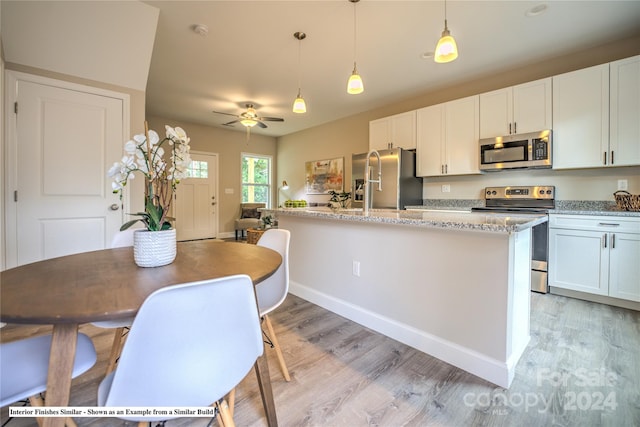 kitchen with light stone countertops, white cabinets, decorative light fixtures, and stainless steel appliances