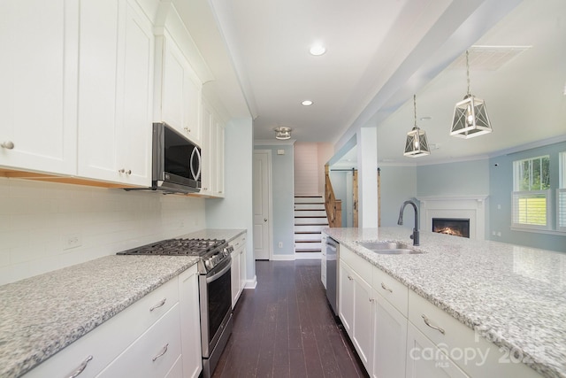 kitchen with sink, white cabinets, decorative light fixtures, light stone counters, and appliances with stainless steel finishes