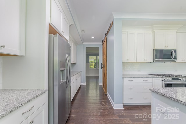 kitchen with appliances with stainless steel finishes, white cabinetry, a barn door, and light stone countertops