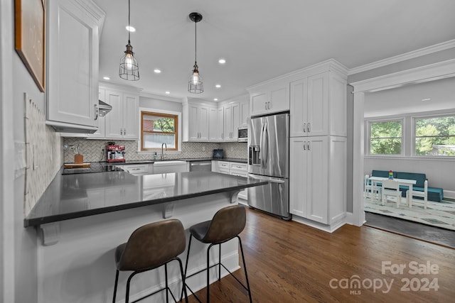 kitchen featuring dark wood-type flooring, hanging light fixtures, stainless steel appliances, a breakfast bar area, and white cabinetry