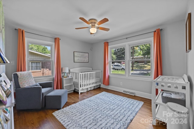 bedroom featuring a crib, dark hardwood / wood-style flooring, and ceiling fan