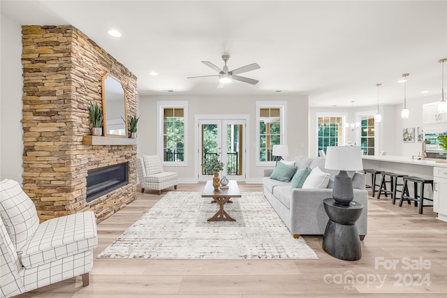 living room with ceiling fan, a stone fireplace, and light wood-type flooring