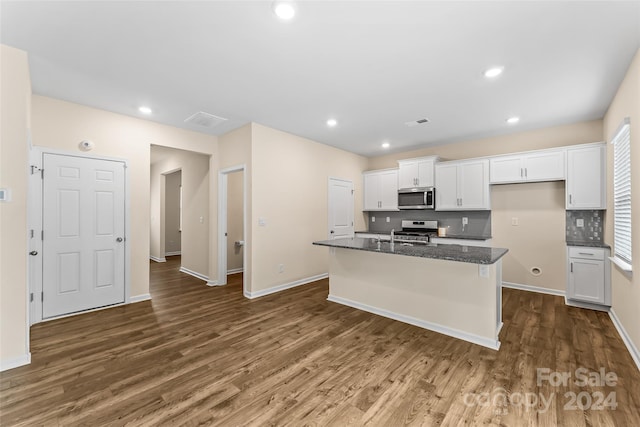 kitchen with appliances with stainless steel finishes, dark stone countertops, white cabinets, and a kitchen island with sink