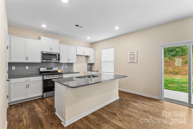 kitchen featuring white cabinetry, a center island with sink, appliances with stainless steel finishes, decorative backsplash, and dark stone countertops