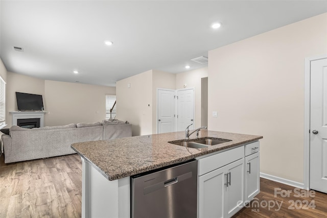 kitchen featuring light stone countertops, white cabinetry, sink, stainless steel dishwasher, and a center island with sink