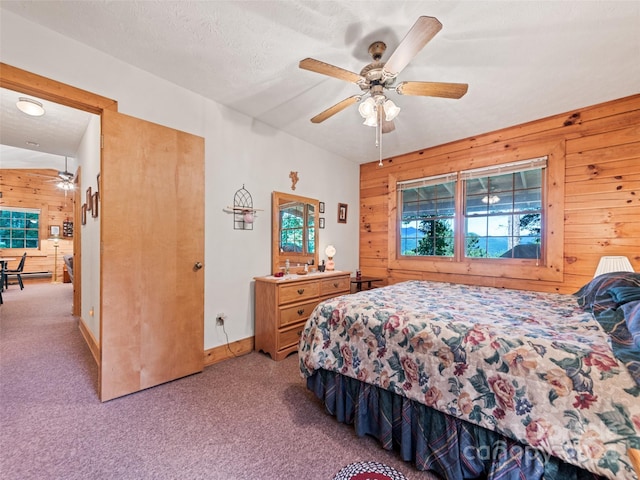 carpeted bedroom featuring a textured ceiling, ceiling fan, and wood walls