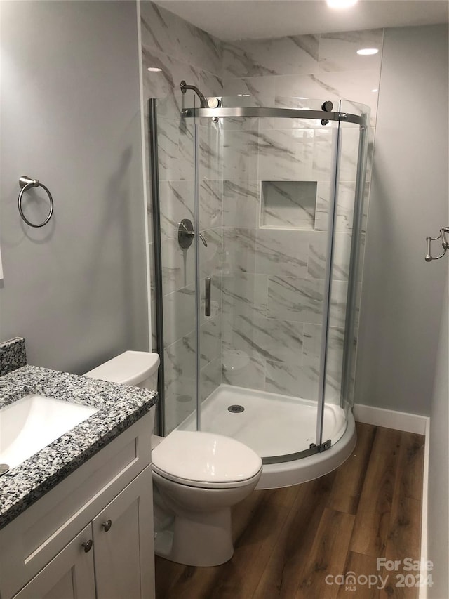 bathroom with hardwood / wood-style floors, vanity, toilet, and a shower with shower door