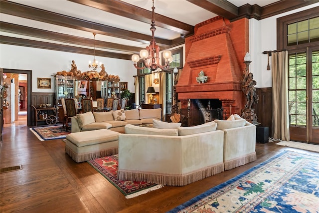 living room featuring a brick fireplace, dark wood-type flooring, beam ceiling, and a chandelier