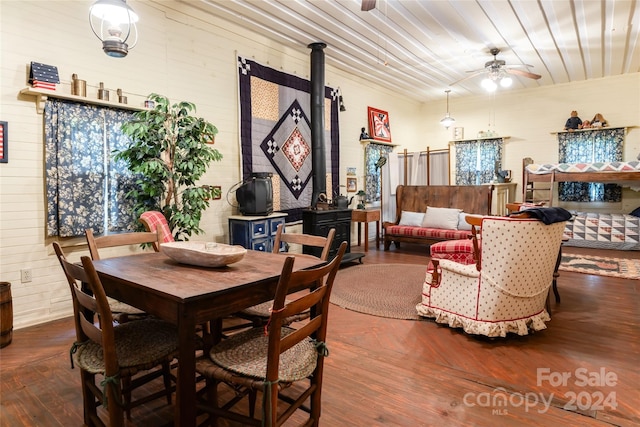 dining area with ceiling fan, a wood stove, and wood-type flooring