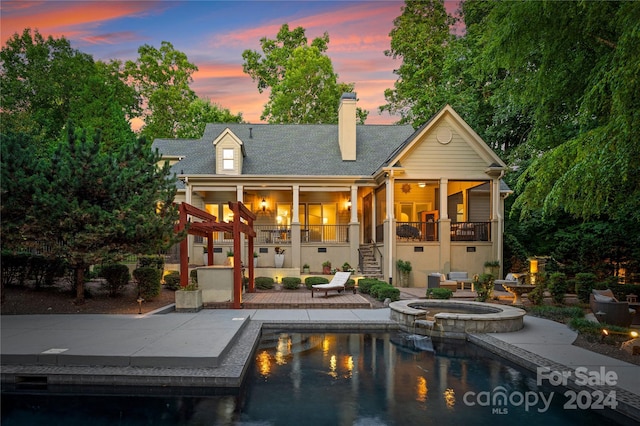 back house at dusk with a swimming pool with hot tub, a balcony, and a patio