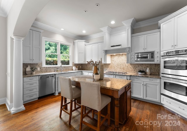 kitchen featuring a kitchen bar, appliances with stainless steel finishes, light stone counters, white cabinets, and a kitchen island