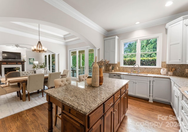 kitchen featuring light stone countertops, sink, light hardwood / wood-style floors, white cabinetry, and hanging light fixtures