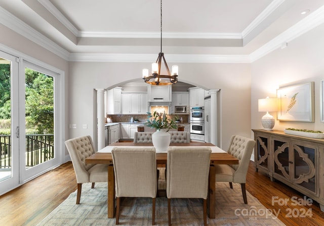 dining room featuring hardwood / wood-style floors, ornate columns, a tray ceiling, and an inviting chandelier