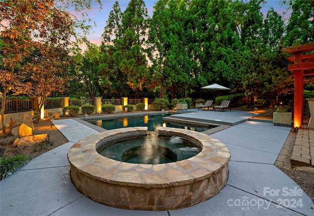 pool at dusk featuring an in ground hot tub and a patio