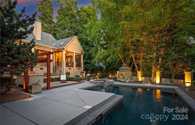 pool at dusk featuring an in ground hot tub, a patio, and exterior fireplace