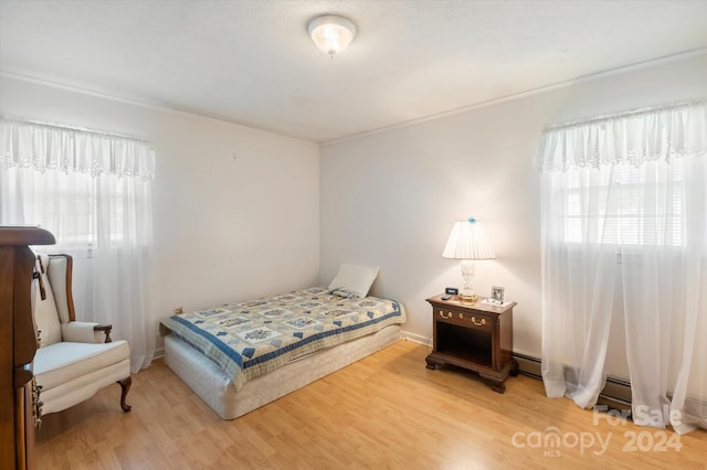 bedroom featuring wood-type flooring, baseboard heating, and multiple windows