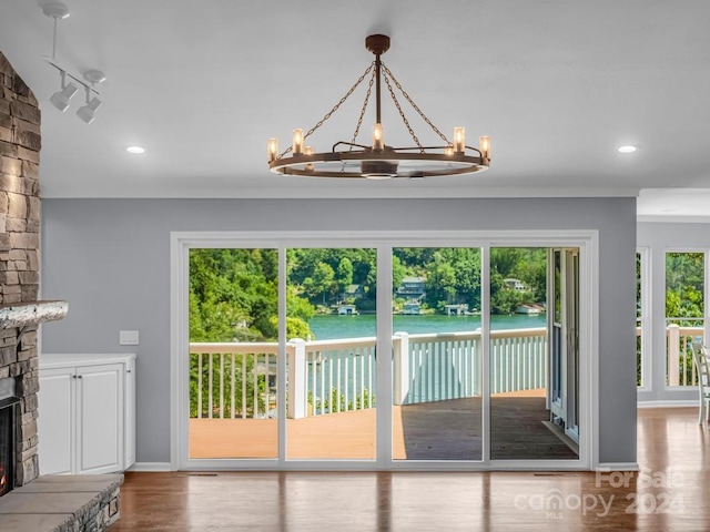 entryway featuring light wood-type flooring, a water view, a stone fireplace, and an inviting chandelier